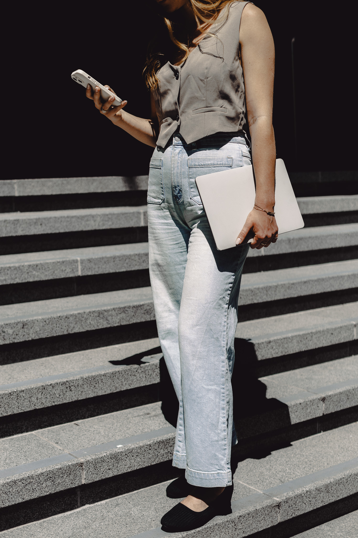 Woman standing on outdoor steps holding a laptop and phone, representing a Christian entrepreneur navigating a slow business season with faith and strategy.