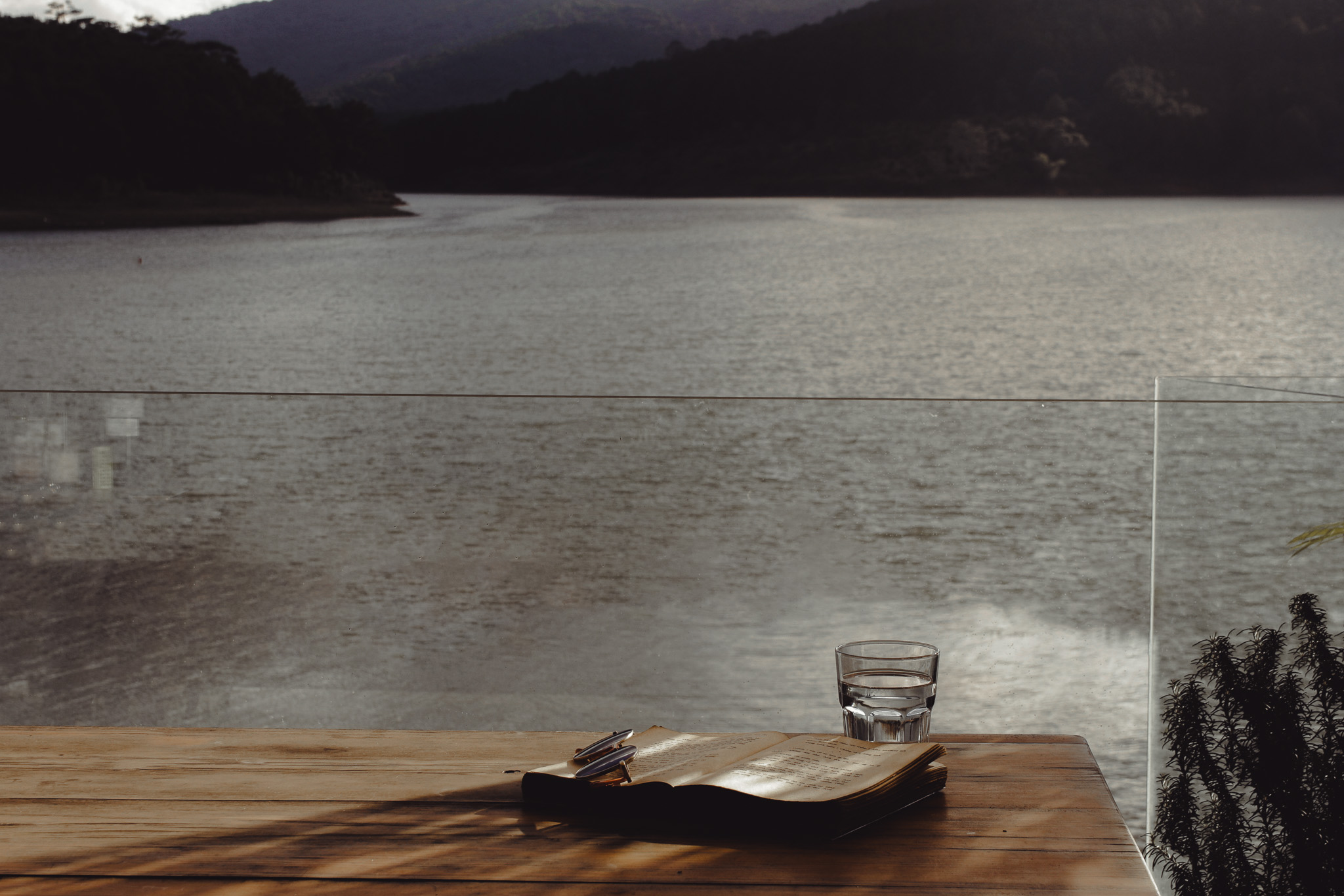 Open Bible and glass of water on a wooden table overlooking still waters — a peaceful setting for soul rest and reflection.