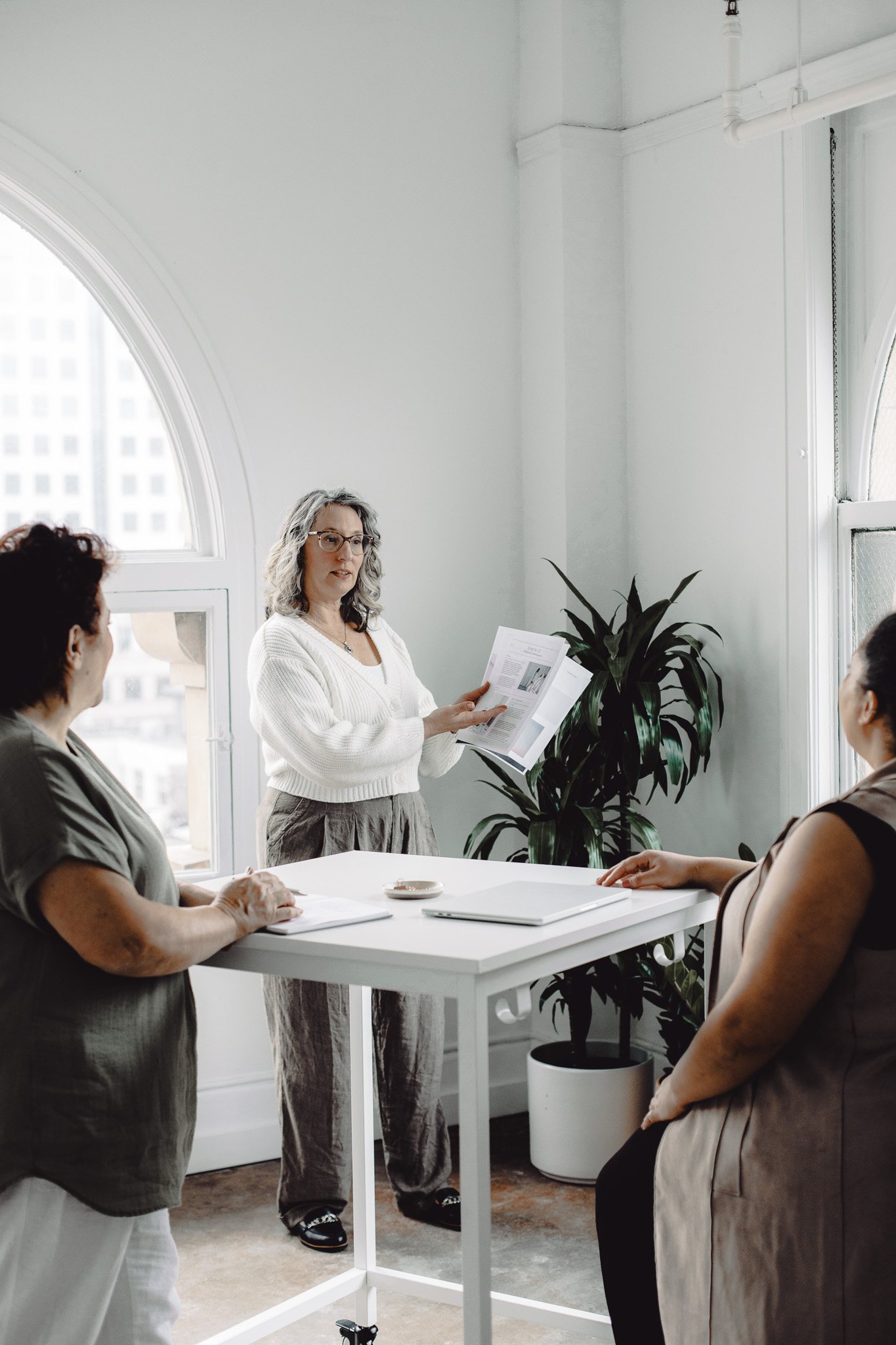 Mature woman leading a business meeting with two other women in a bright modern office.