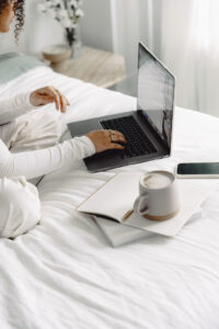 “Woman working on laptop in bed with coffee and notebook, planning how to grow her email list”