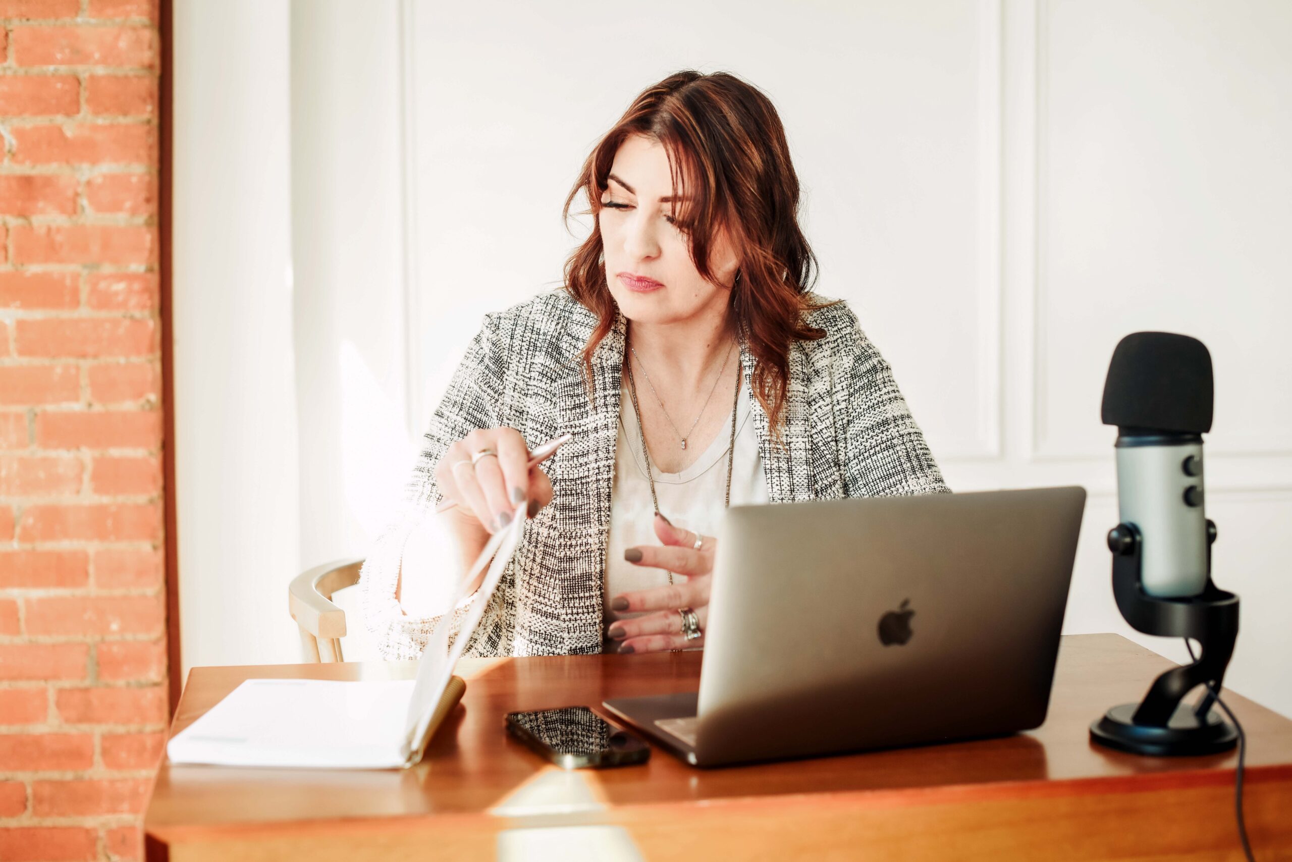 Jan Touchberry at her desk recording a podcast with a microphone, laptop, and notes in front of her