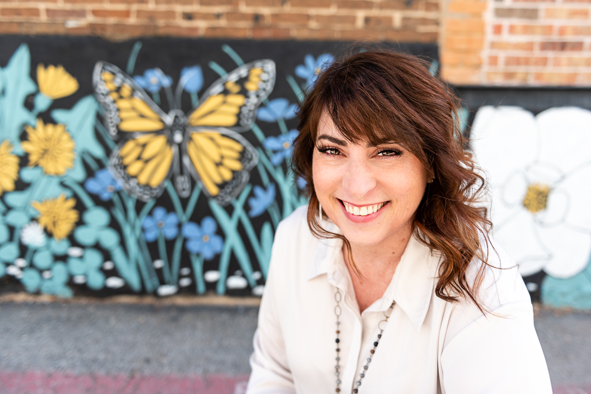 Jan Touchberry smiling in front of a mural with a yellow butterfly and wildflowers, representing faith-based entrepreneurship and joyful leadership.