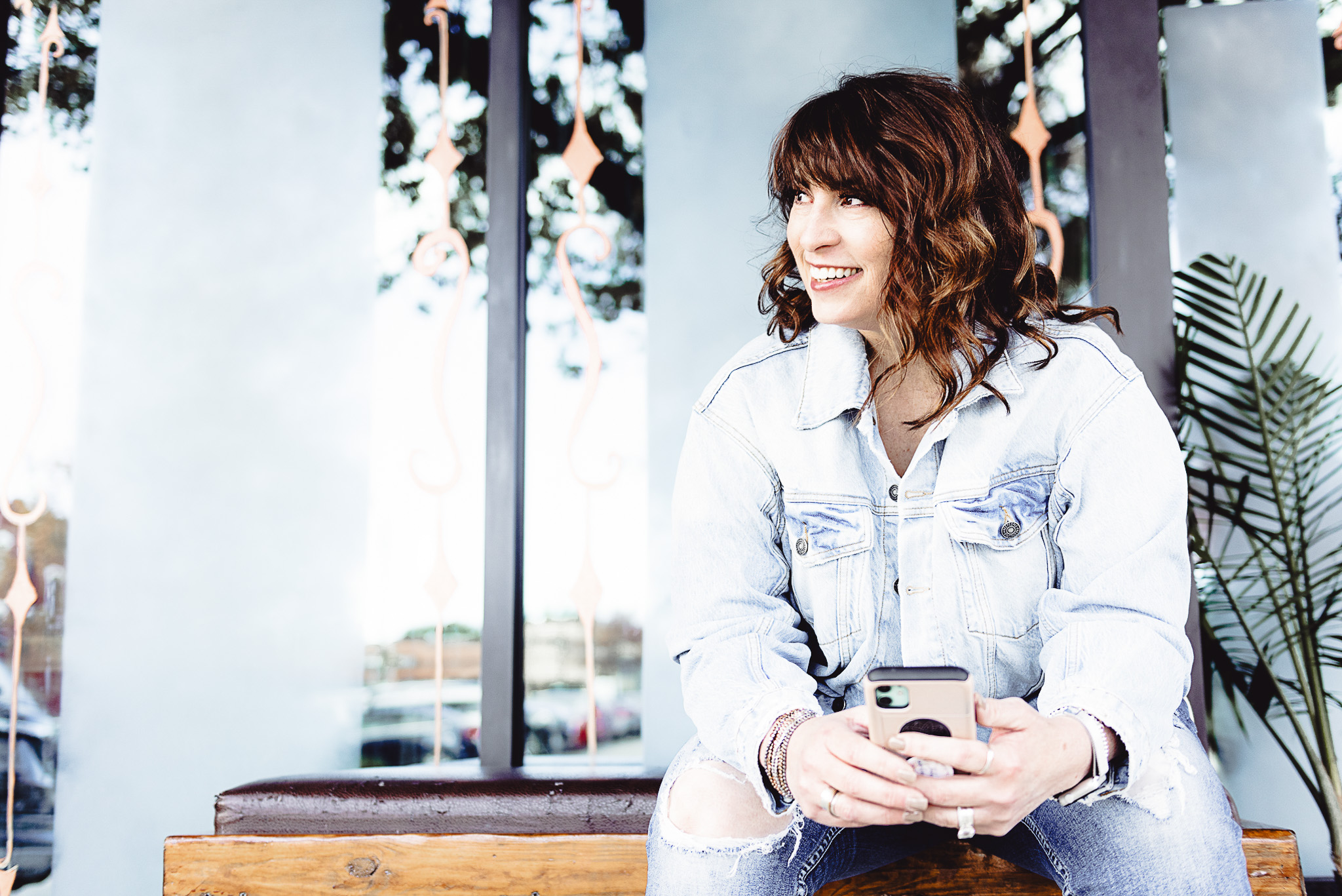 Jan Touchberry smiling and holding a phone, seated outside in a light denim jacket