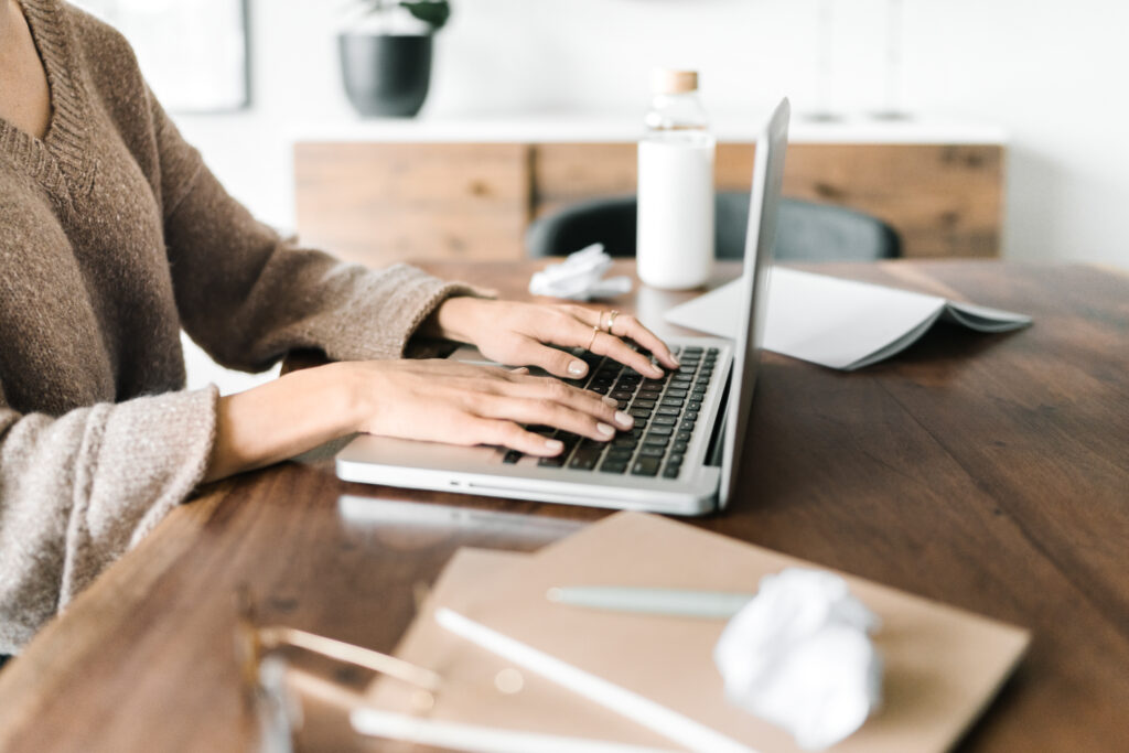 Woman typing on laptop at wooden desk with notebook and pen, working on SEO and business growth strategy for a faith-based business.