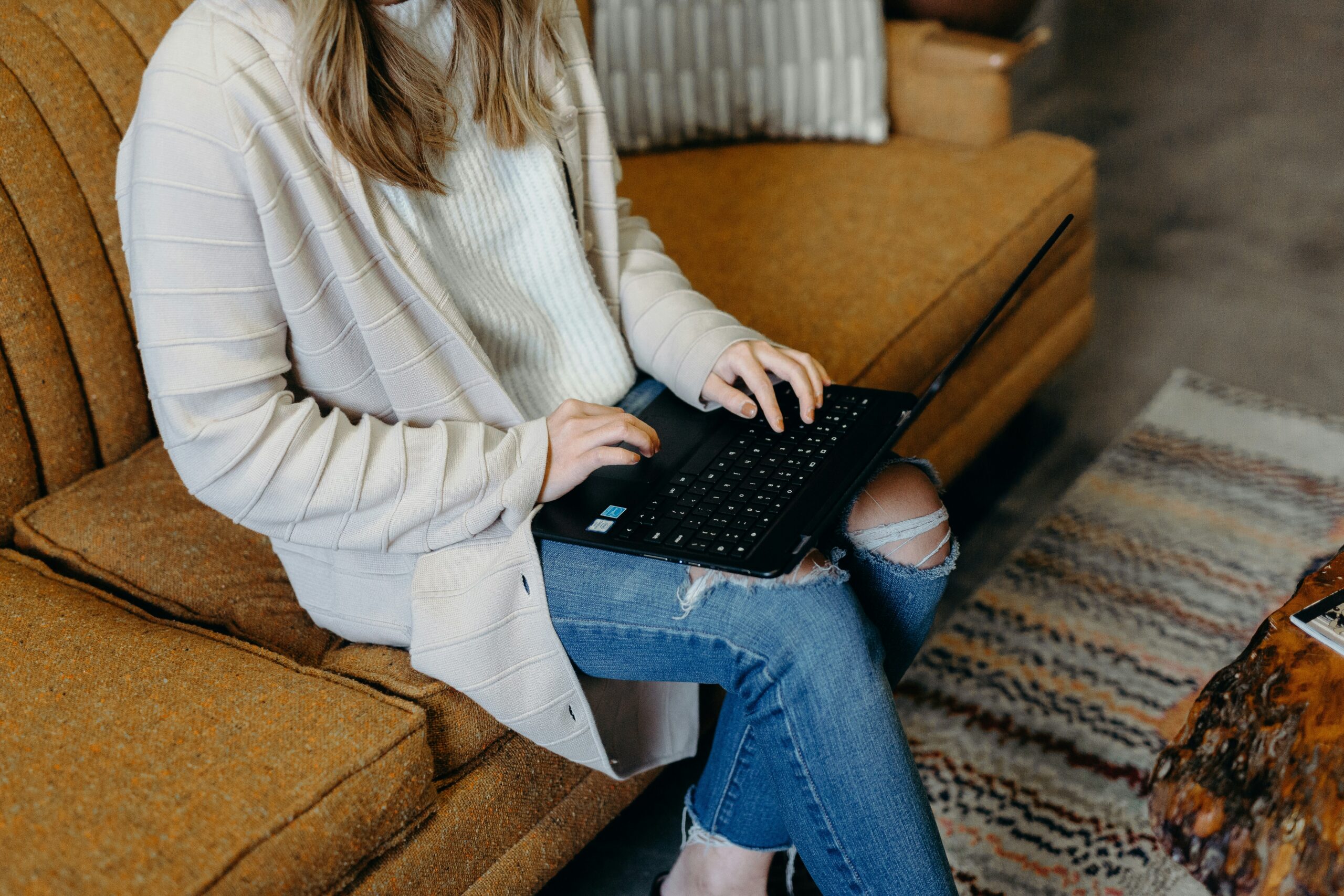 Person sitting on a couch working on a laptop, writing or reviewing content for business visibility and online strategy.