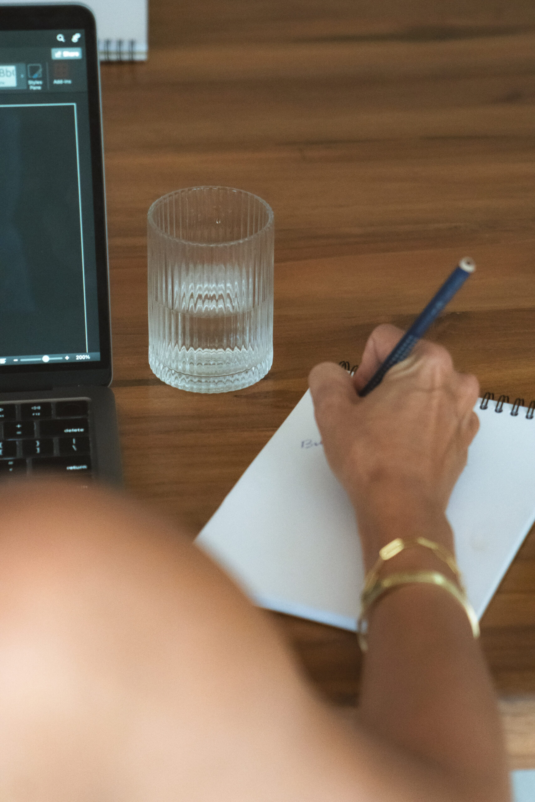 Woman writing in a notebook beside her laptop to protect her brand voice while using AI